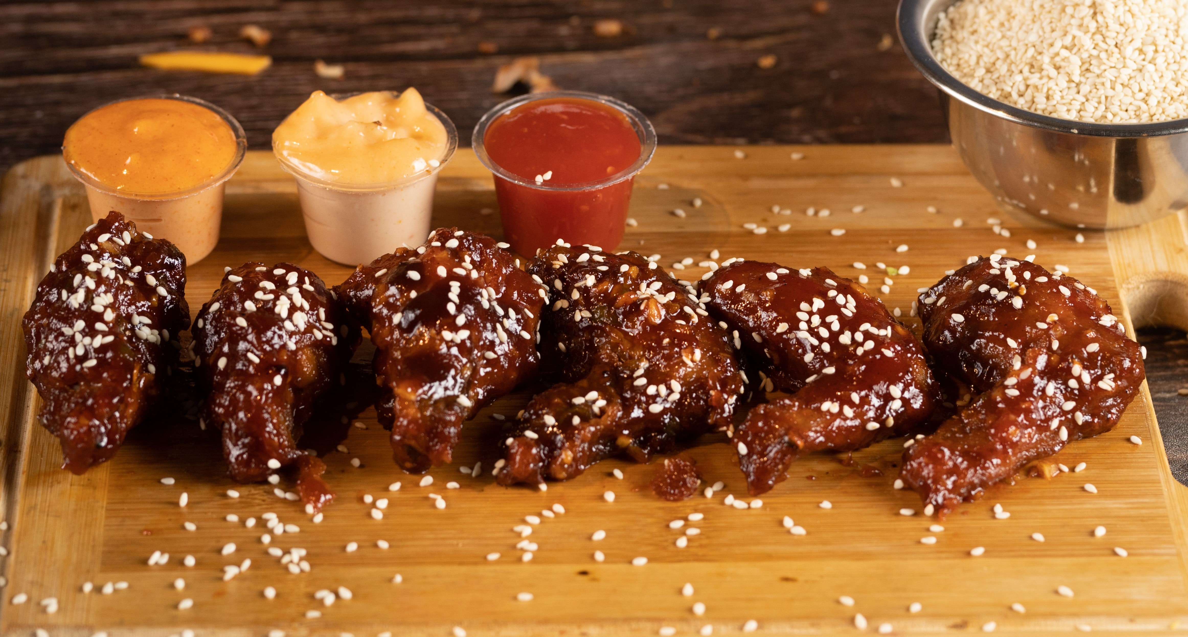 Wings laying on a cutting board with sauces behind them